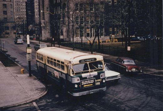 A green and cream Chicago Transit Authority bus, number 8480, is parked at a street corner in winter, with a 'Union Station via Ohio' destination sign. Classic cars are visible on the wet street, and a large stone building stands in the background.