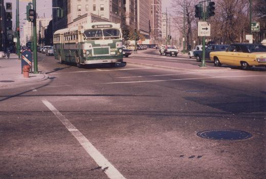 A green and cream CTA bus, number 8336 on route 36 Broadway-Downtown, turns at a city street intersection lined with 1970s cars and tall buildings.
