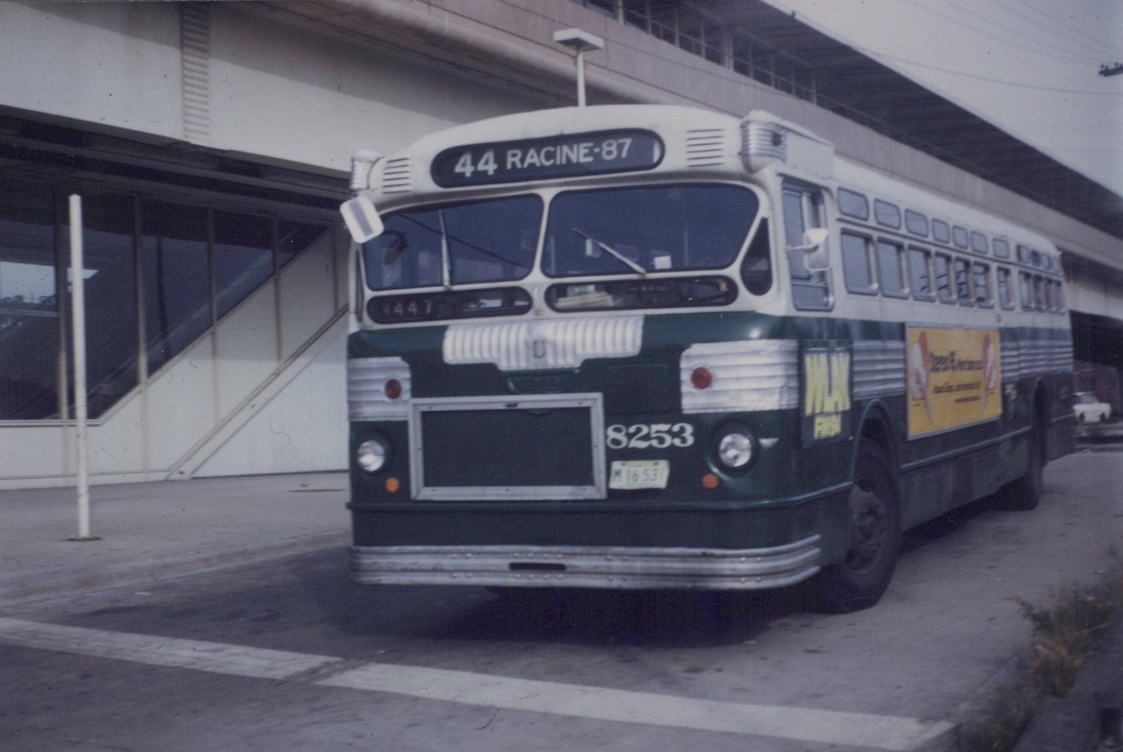 A green and white Chicago Transit Authority bus, number 8253, on route 44 Racine-87, parked on a street under an elevated structure.