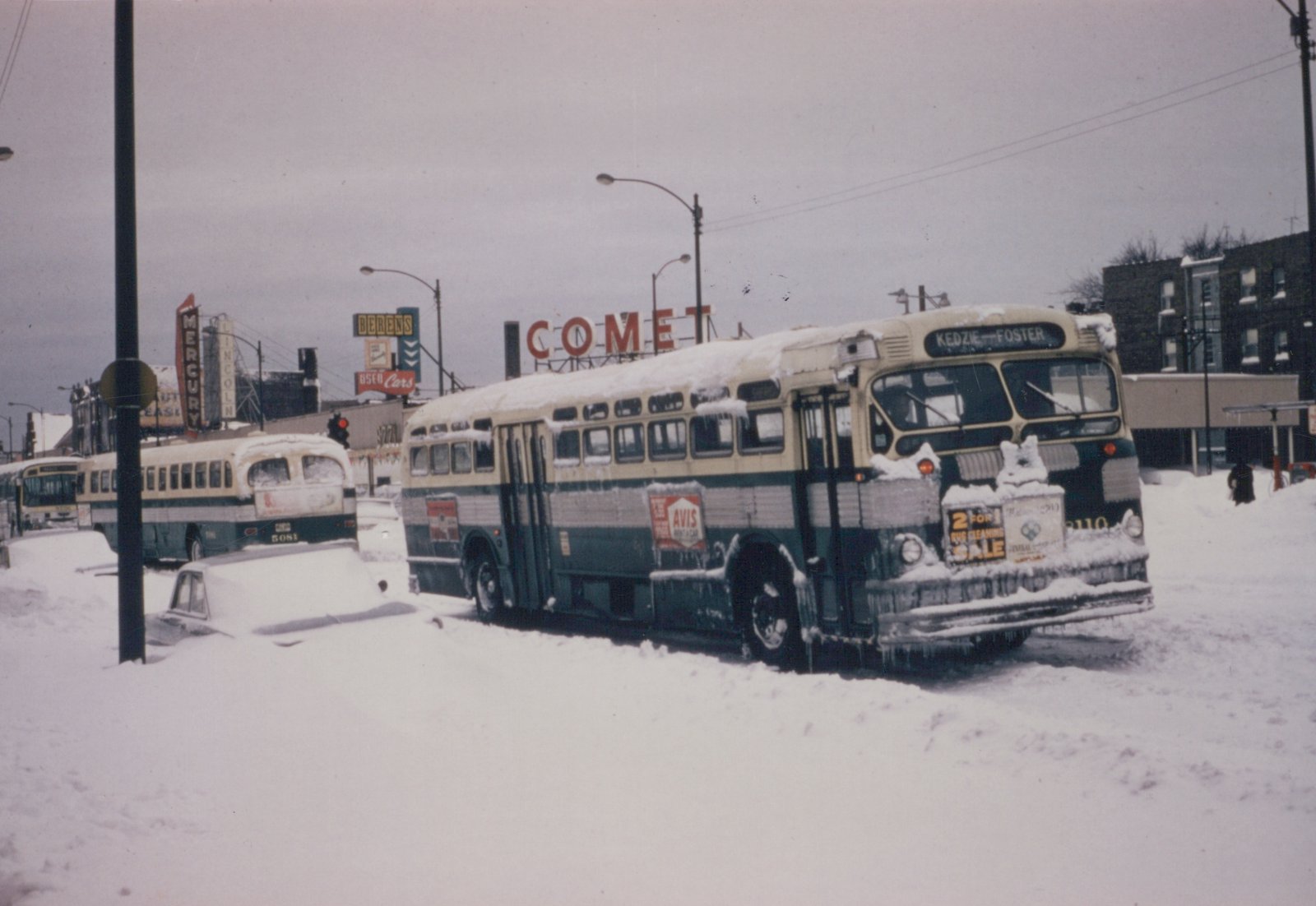 A winter scene with two snow-covered Chicago Transit Authority buses on a city street, one showing destination Kedzie-Foster and number 2110, with billboards and a snow-covered car nearby.
