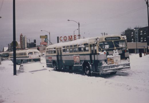 A winter scene with two snow-covered Chicago Transit Authority buses on a city street, one showing destination Kedzie-Foster and number 2110, with billboards and a snow-covered car nearby.