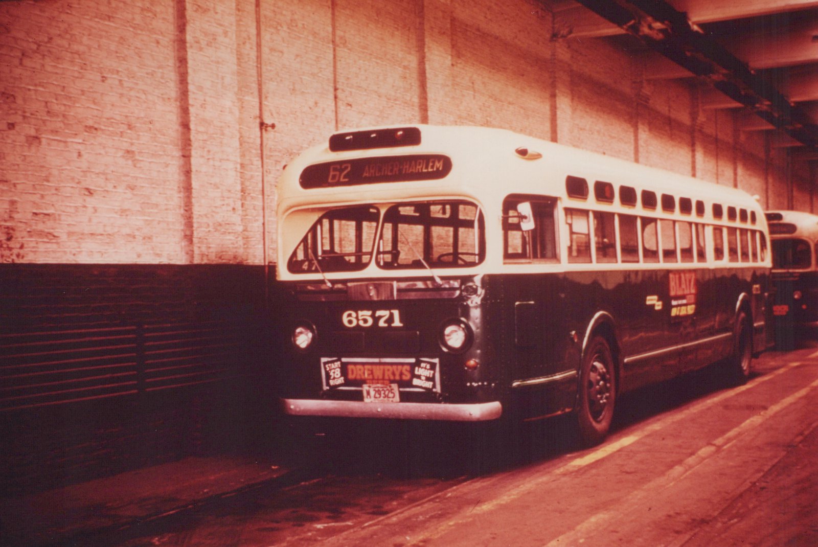 A vintage Chicago Transit Authority bus, number 6571, is parked under a brick archway, displaying route 62 Archer-Harlem on its front sign and advertisements for Drewry's and Blatz beer on its bumper and side.
