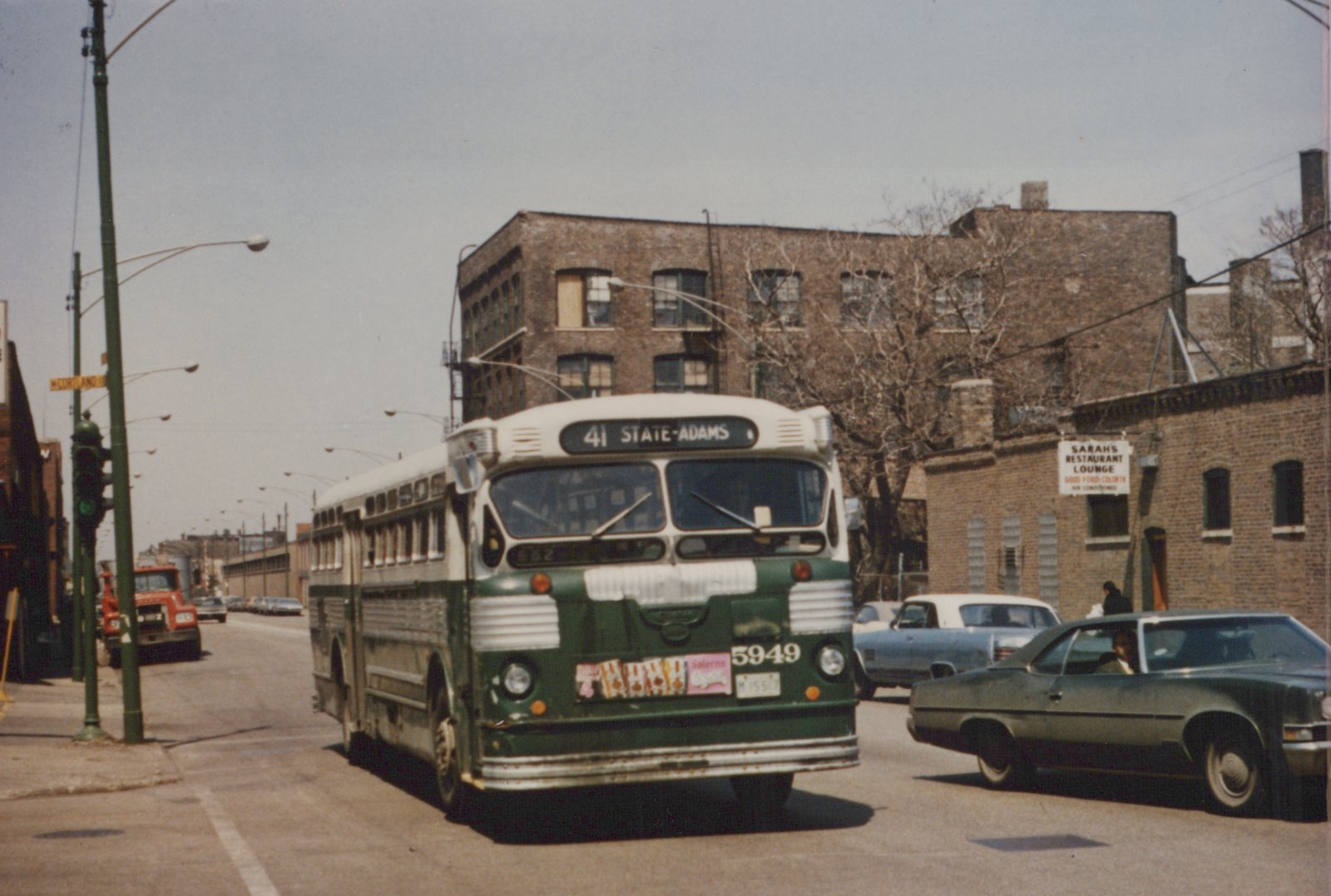 Green and cream CTA bus number 5949 on the 41 State-Adams route at a street intersection with brick buildings and cars in the background.
