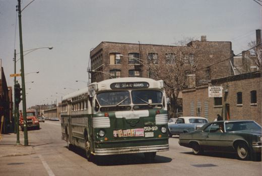 Green and cream CTA bus number 5949 on the 41 State-Adams route at a street intersection with brick buildings and cars in the background.