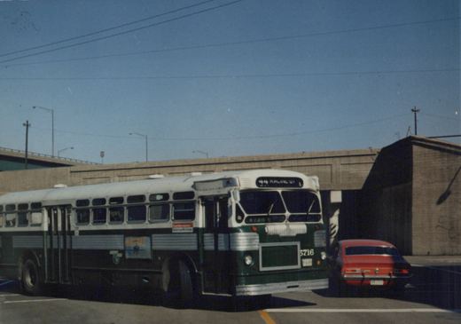 A green and cream Chicago Transit Authority bus, number 5716, is parked on a sunny day with a red car nearby and a concrete overpass in the background.
