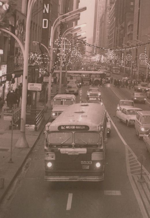 A black and white photo of a Chicago Transit Authority bus, number 5533, on the 62 Archer-Harlem route, driving through a crowded city street lined with decorated trees and tall buildings.