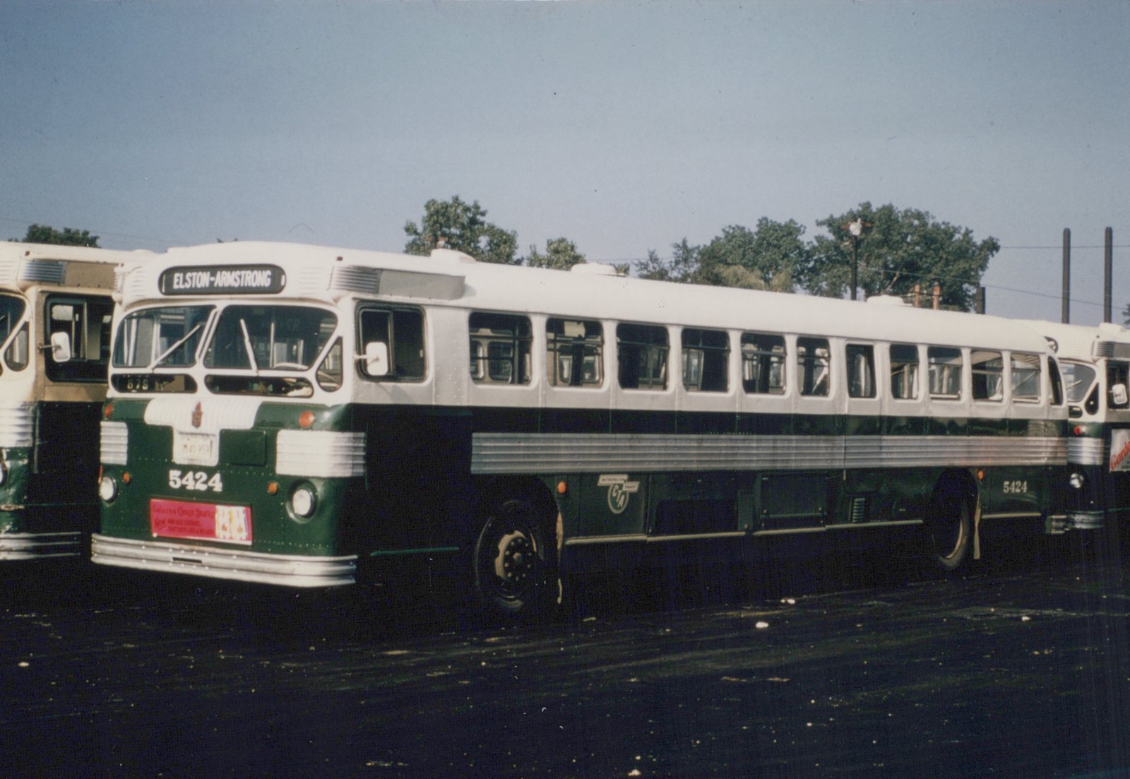 Side view of a green and white Chicago Transit Authority bus, number 5424, parked in a yard with trees and a clear sky in the background.