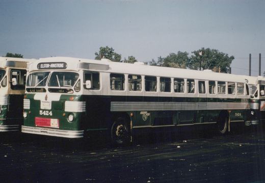 Side view of a green and white Chicago Transit Authority bus, number 5424, parked in a yard with trees and a clear sky in the background.