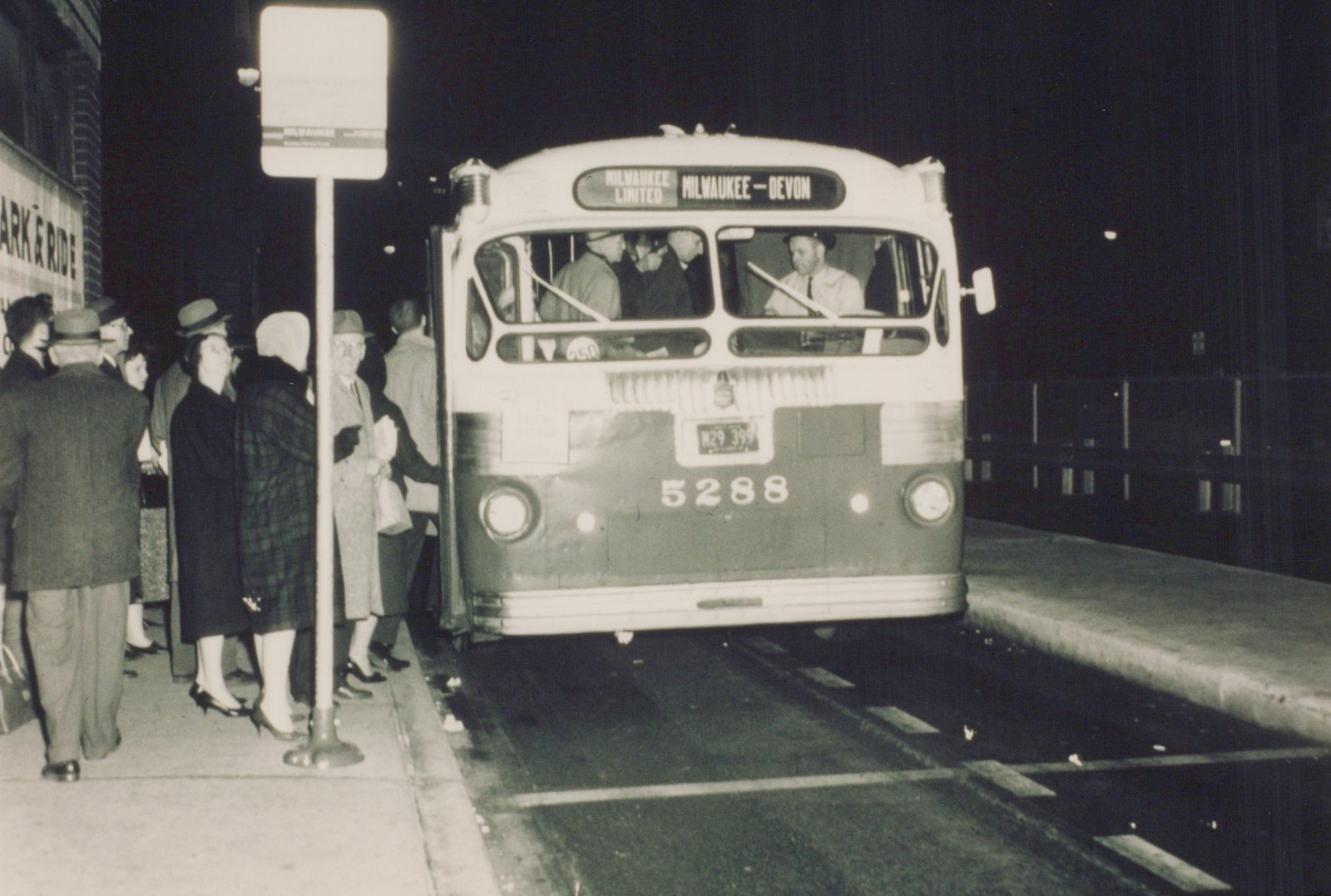 A black and white nighttime photograph of a CTA bus numbered 5288 with destination sign reading 'MILWAUKEE LIMITED MILWAUKEE - DEVON', as passengers board from a sidewalk.