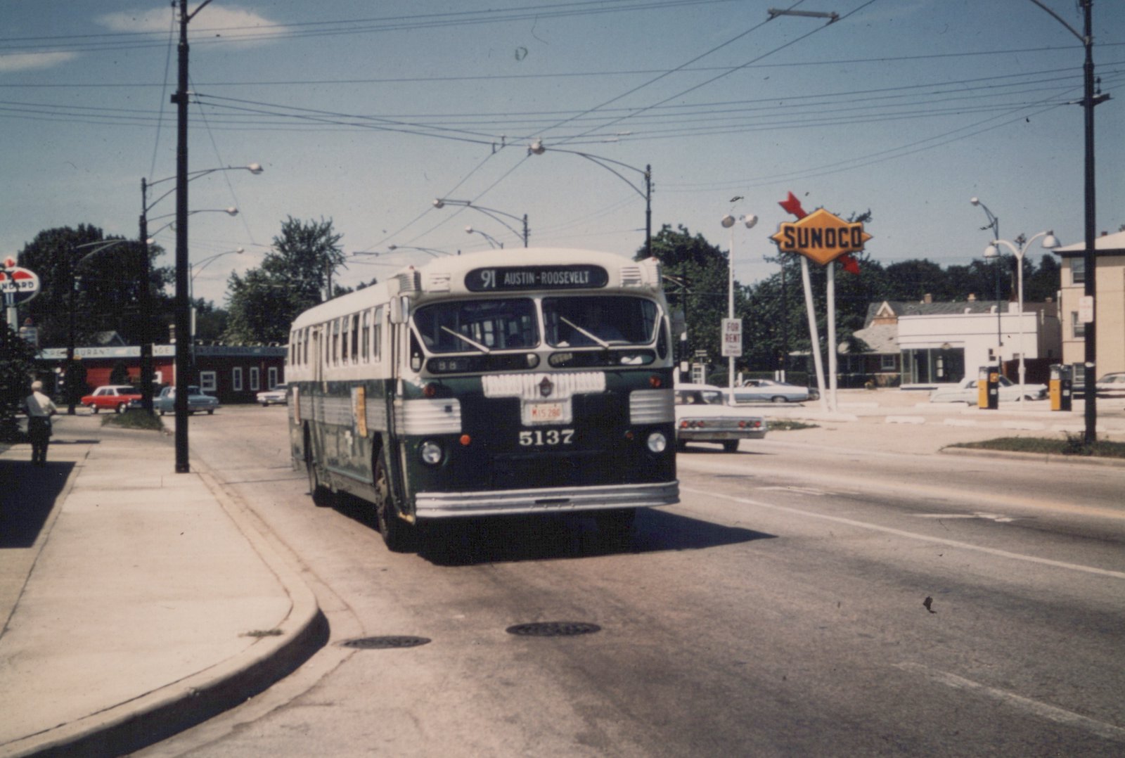 A vintage Chicago bus, number 5137, is shown from a three-quarter front angle on a city street, with overhead wires, a Sunoco gas station sign, and several 1960s cars in the background.
