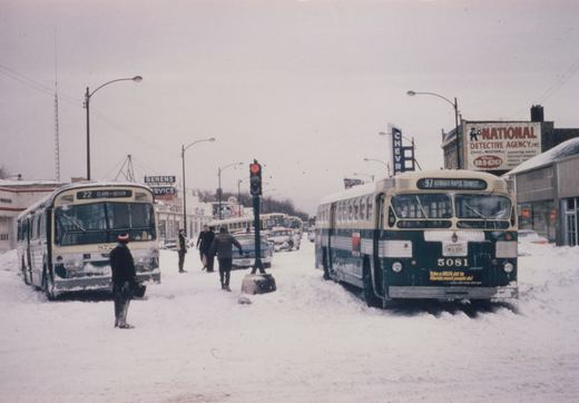 Two vintage CTA buses in a snowy Chicago street scene with several people and other vehicles in the background.