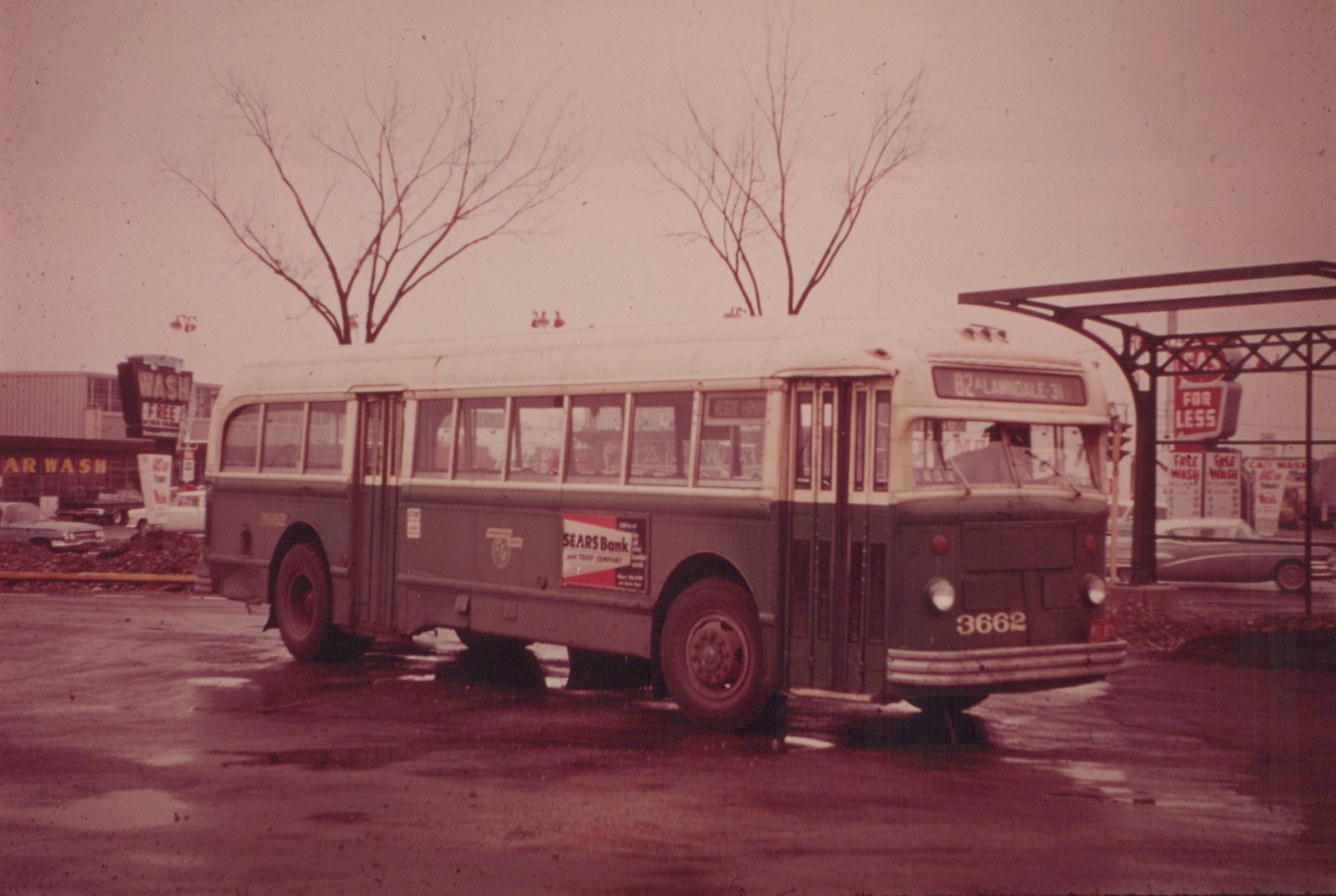 A vintage CTA bus with the number 3662 on its front, parked on a street with wet pavement in winter, with a car wash and bare trees visible in the background.