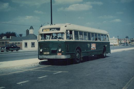 A green and cream CTA bus numbered 3639 is driving down a city street on an overcast day, with a vintage car parked across the street.