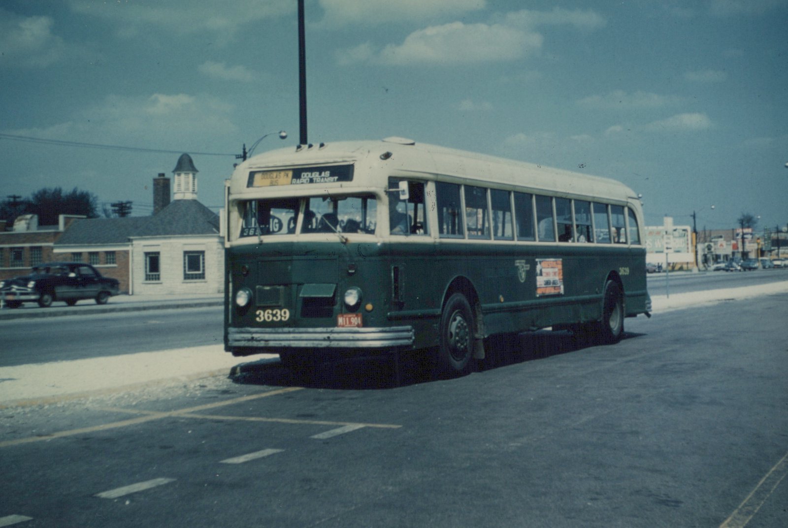 A green and cream CTA bus numbered 3639 is driving down a city street on an overcast day, with a vintage car parked across the street.