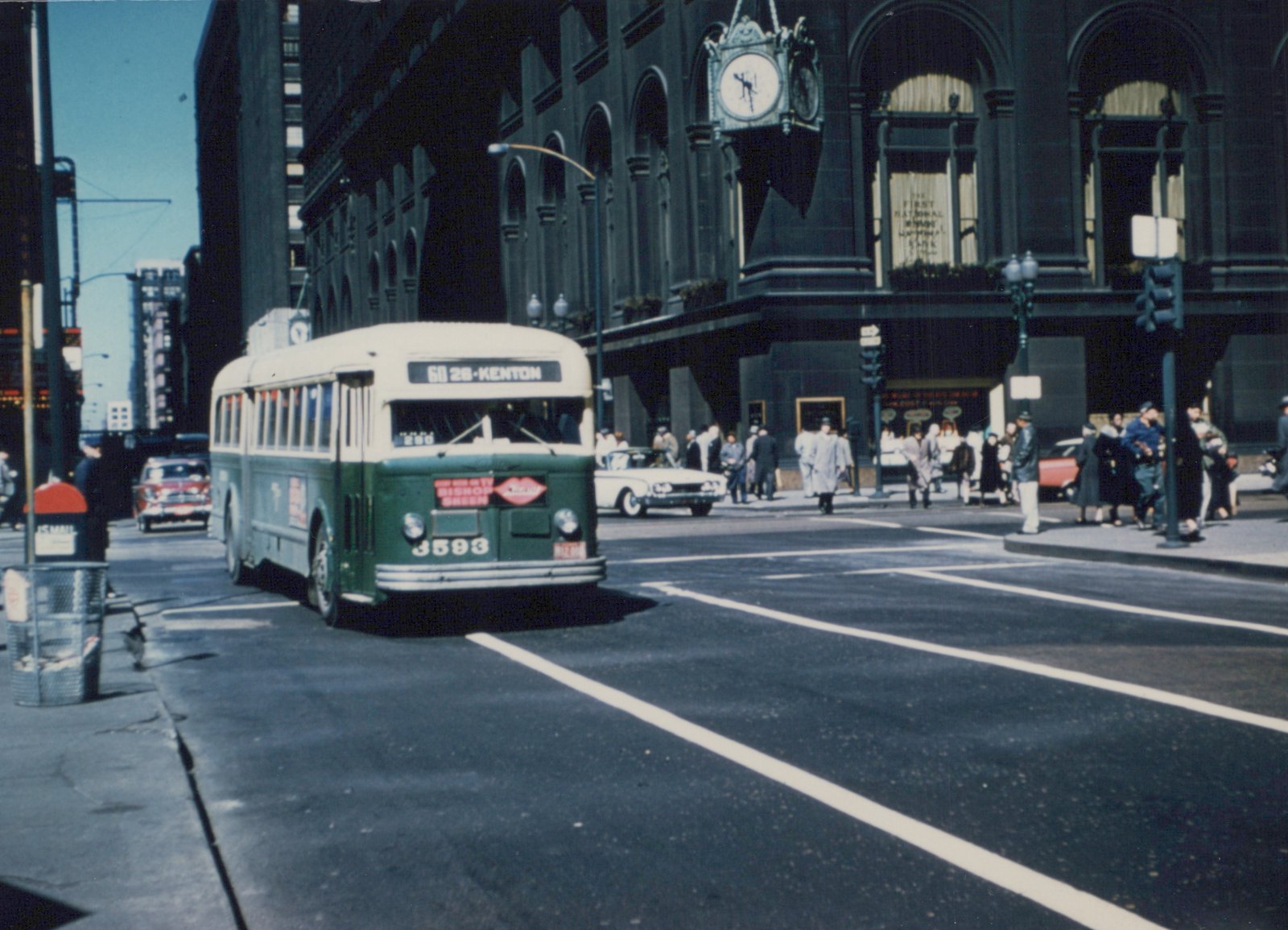 A green and cream Chicago Transit Authority bus, number 3593, is turning at a downtown intersection with pedestrians and classic cars nearby, under a clear blue sky.
