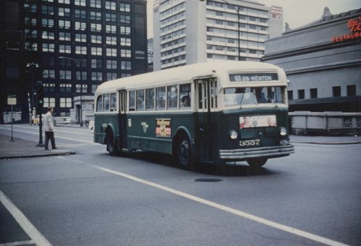 A green and cream Chicago Transit Authority bus, number 3557, on a city street with tall buildings in the background.