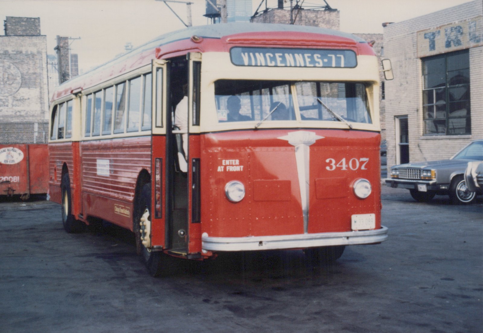 A red and cream CTA bus from the 1970s, number 3407, is parked on a street, its front roll sign reading Vincennes-77.