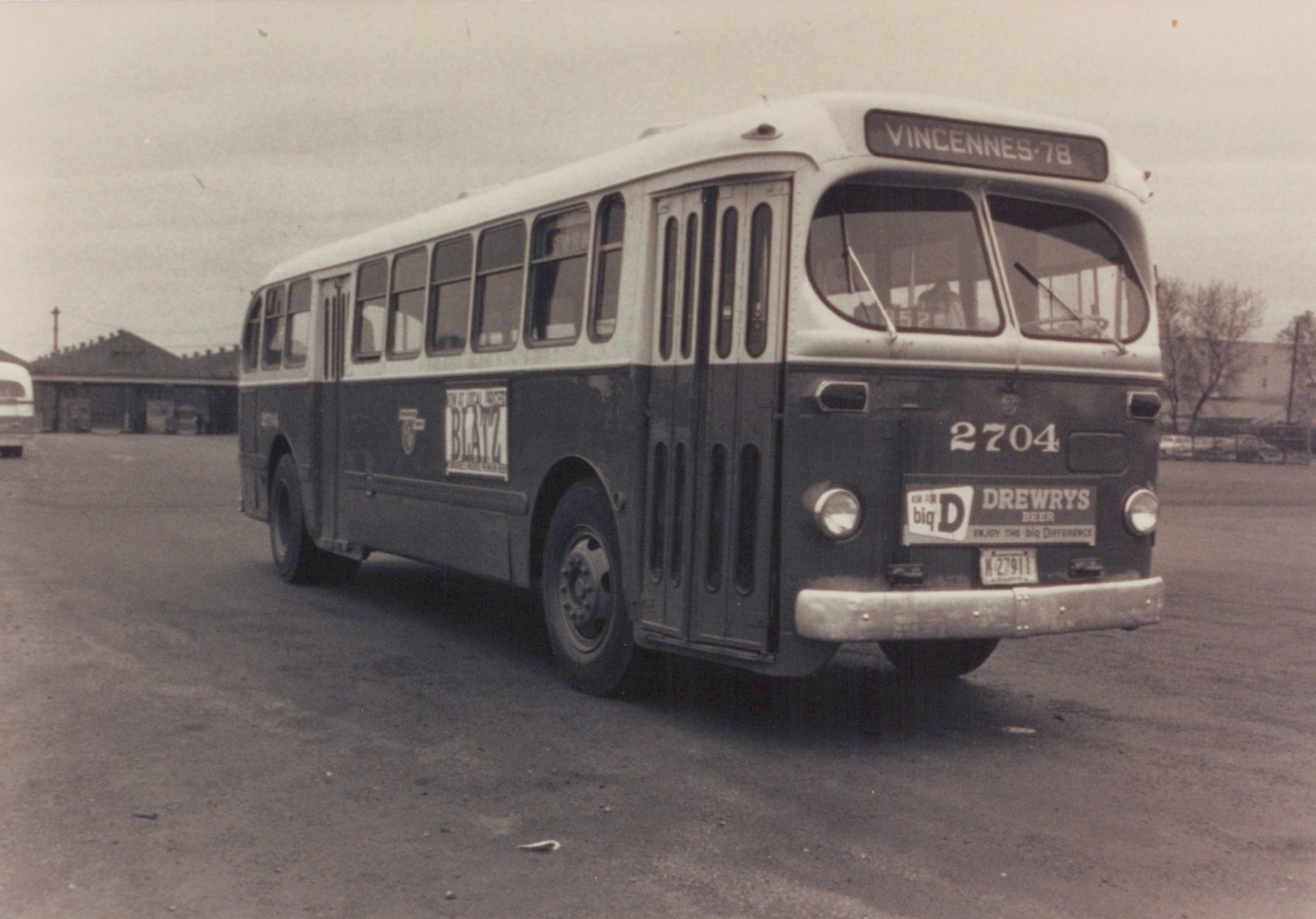 A dark blue and cream CTA bus, number 2704, with a Vincennes-78 route sign and Drewry's Beer advertisement on the front, parked on a paved lot with a building in the background.