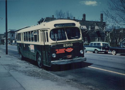 A vintage CTA bus numbered 2503 is parked on a city street, displaying a route sign for '58 25 LARAMIE' and an ad for 'Magikist' dry cleaners, with 1950s cars in the background.