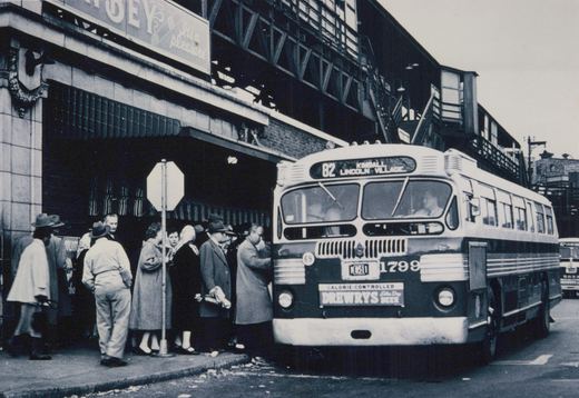A black-and-white photograph of a vintage Chicago CTA bus, number 1799, stopped on a city street with a group of people waiting to board. The bus displays a route sign for '82 Kimball Lincoln Village' and a 'Drewry's Beer' advertisement on the front. An elevated train structure looms overhead.