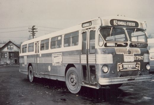 A black and white photo of a Chicago Transit Authority motor bus, number 1787, showing its front and side with route signs and advertisements, parked on a wet street with a house in the background.