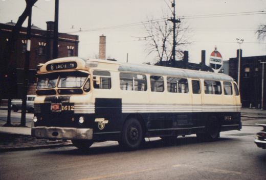A cream and dark green CTA bus with the number 1612 on its front and rear, showing the destination '6 LAKE-AUSTIN' on its sign, driving down a street with a Standard Oil sign and bare trees in the background.