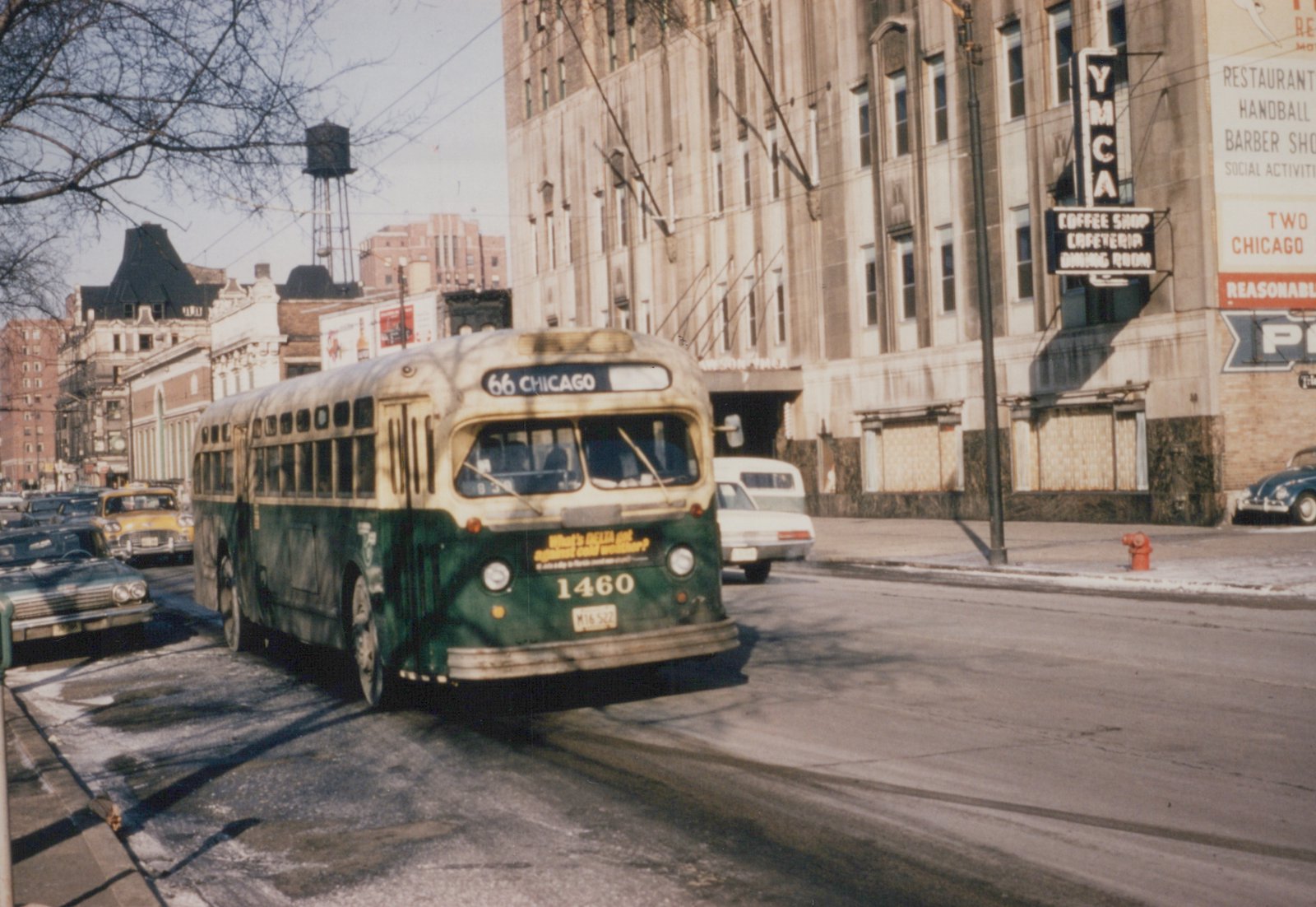 A vintage green and cream Chicago Transit Authority bus, number 1460, is driving down a city street with snow on the ground, with a YMCA building and other cars in the background.