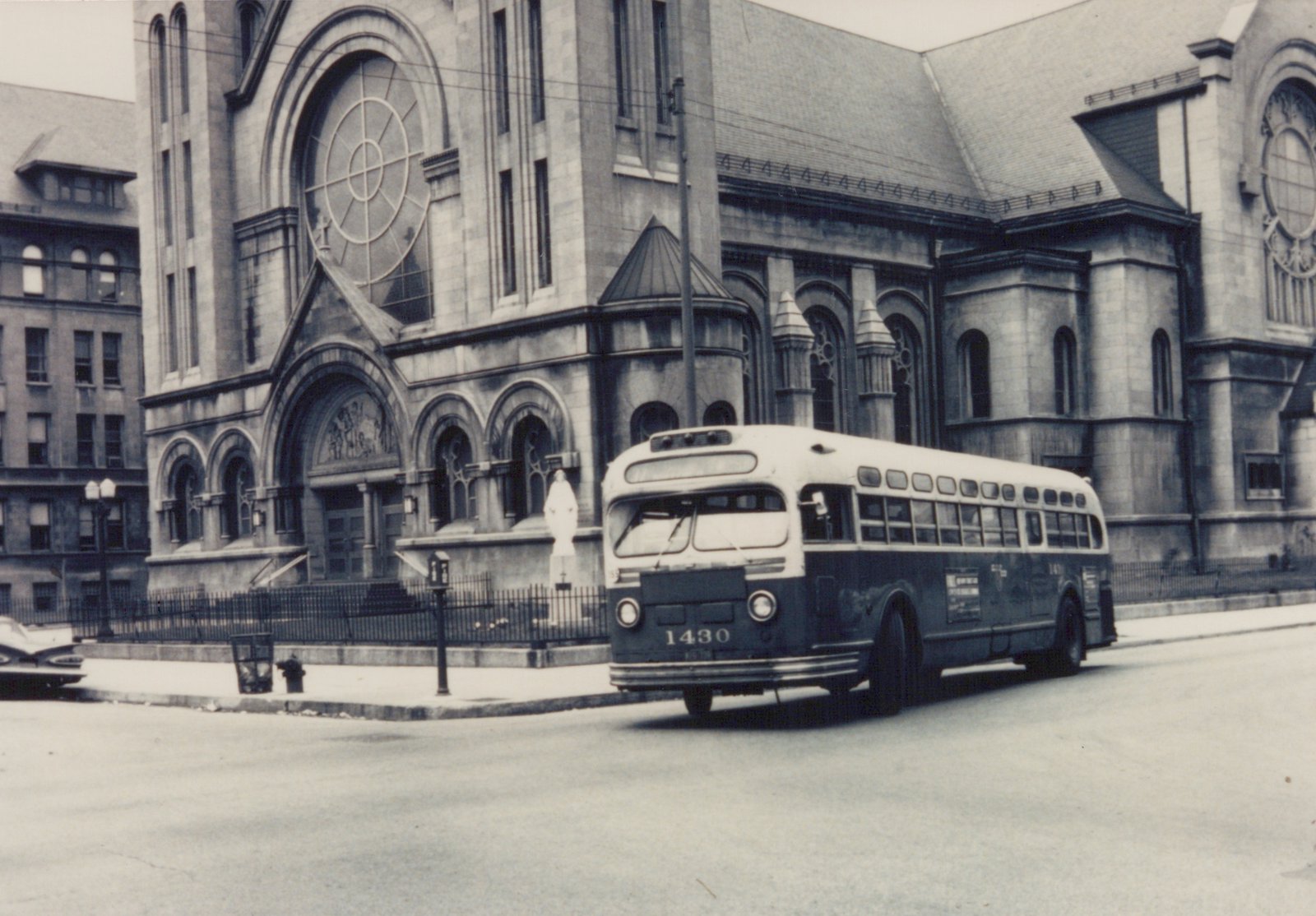 A vintage black and white photo of a Chicago Transit Authority bus, number 1430, on a street in front of a stone church with arched windows and a statue on its steps.
