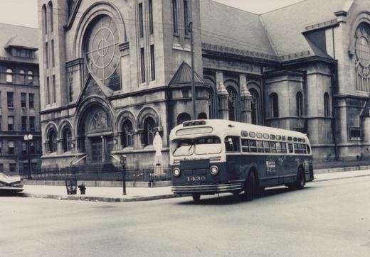 A vintage black and white photo of a Chicago Transit Authority bus, number 1430, on a street in front of a stone church with arched windows and a statue on its steps.