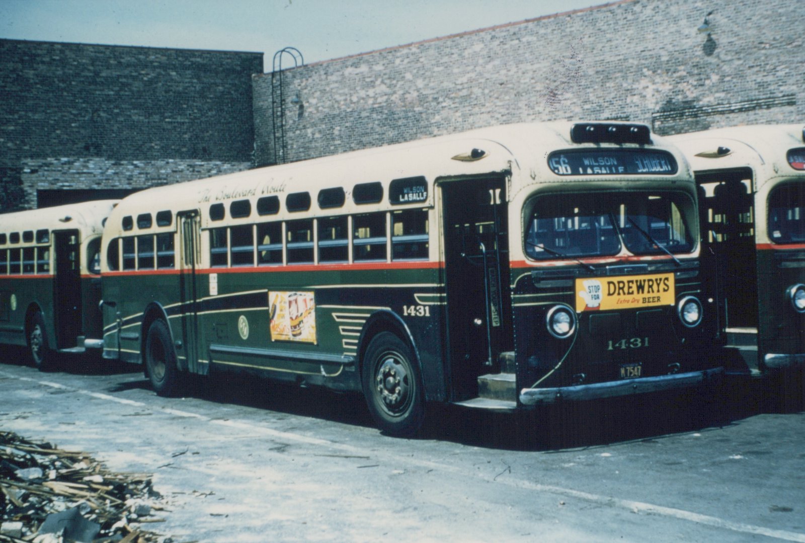 A vintage green and cream motor bus, number 1431, with a 'Drewry's Beer' ad parked on a street, its destination sign reading 56 Wilson La Salle Schubert.