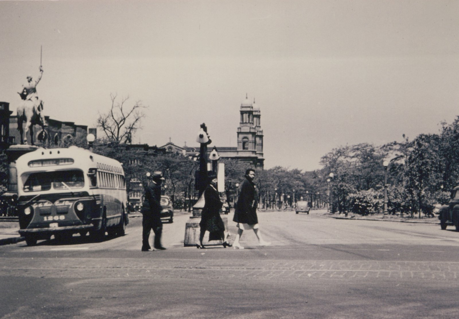 Black and white photograph of a Chicago Surface Lines motor bus, number 1268, stopped at an intersection with pedestrians crossing and a statue of a mounted rider in the background.