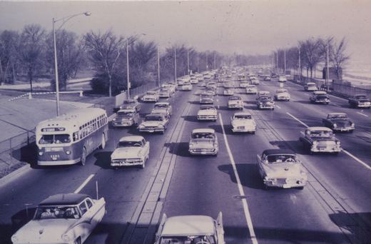 A black and white photo of a Chicago Transit Authority bus with the number 1181 and destination '63 STONEY ISLAND' driving on a multi-lane expressway filled with 1950s cars and surrounded by bare trees.