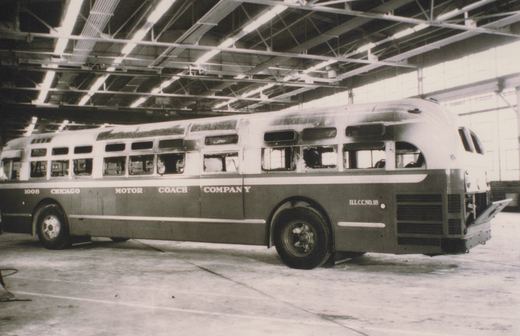 A side view of a Chicago Motor Coach Company bus, numbered 1008, parked inside a large bus garage with its engine compartment open.