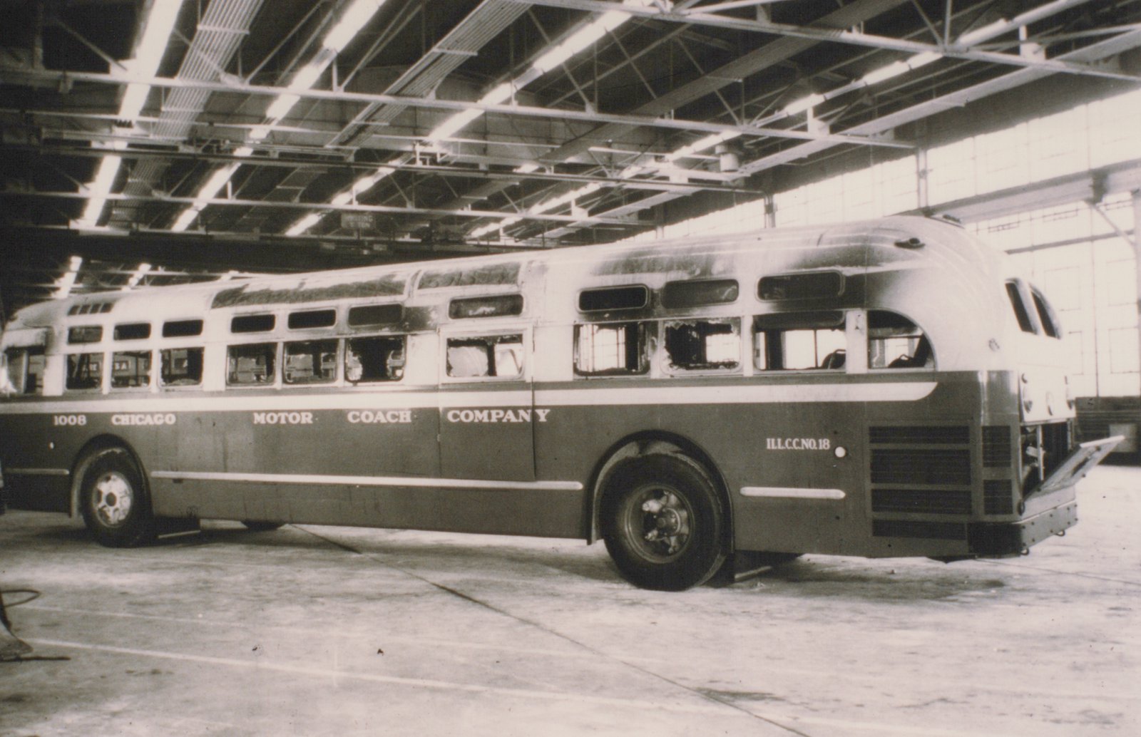 A side view of a Chicago Motor Coach Company bus, numbered 1008, parked inside a large bus garage with its engine compartment open.
