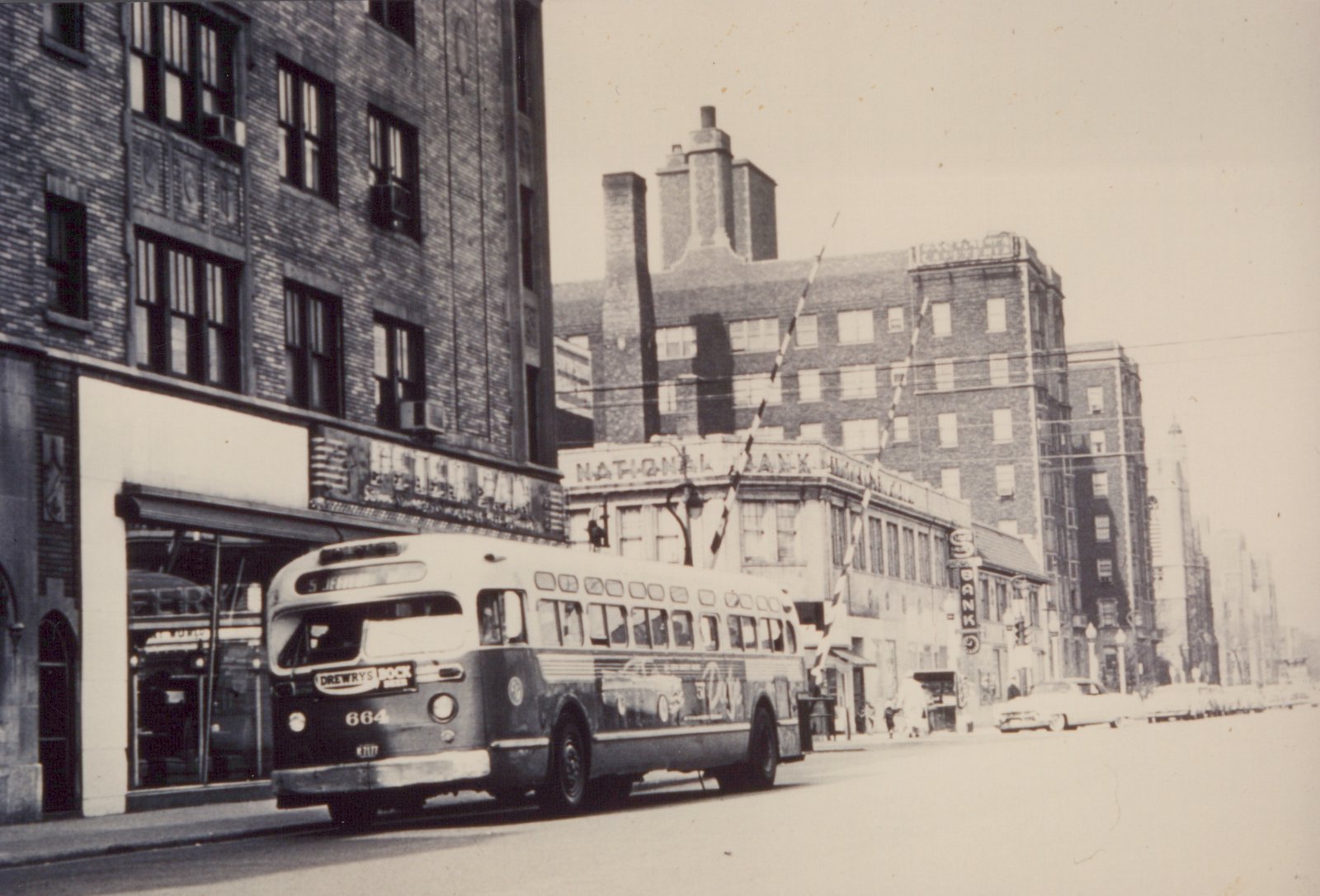 A vintage black-and-white photo of a CTA bus, number 664, on a street with brick buildings and a 'National Bank' sign in the background.