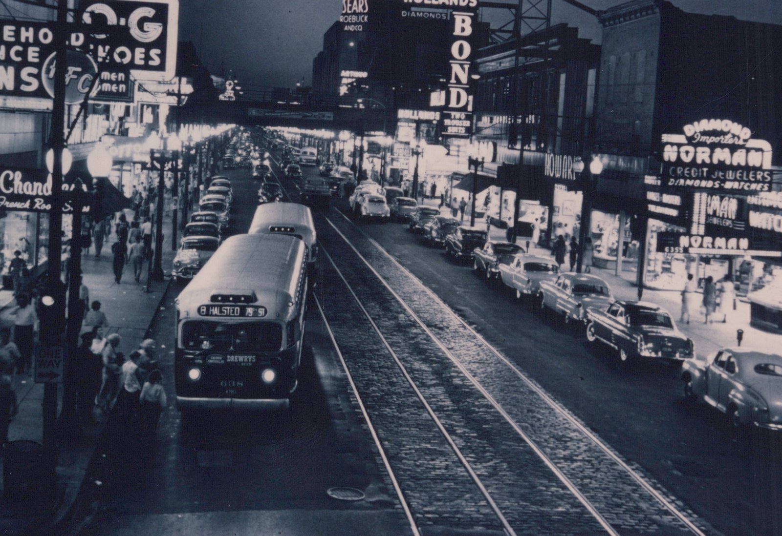 A black and white photo shows a vintage CTA bus labeled '8 HALSTED 79TH ST' and number 638 on a city street at dusk, surrounded by parked cars, pedestrians, and glowing signs for businesses like Sears and Norman Jewelers. The street has embedded trolley tracks, and the scene is bustling with activit