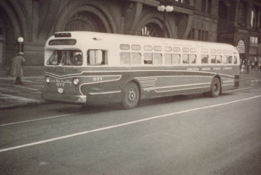 A black and white photo of a vintage Chicago Motor Coach Company bus, number 577, parked on a city street with a person in a coat nearby.