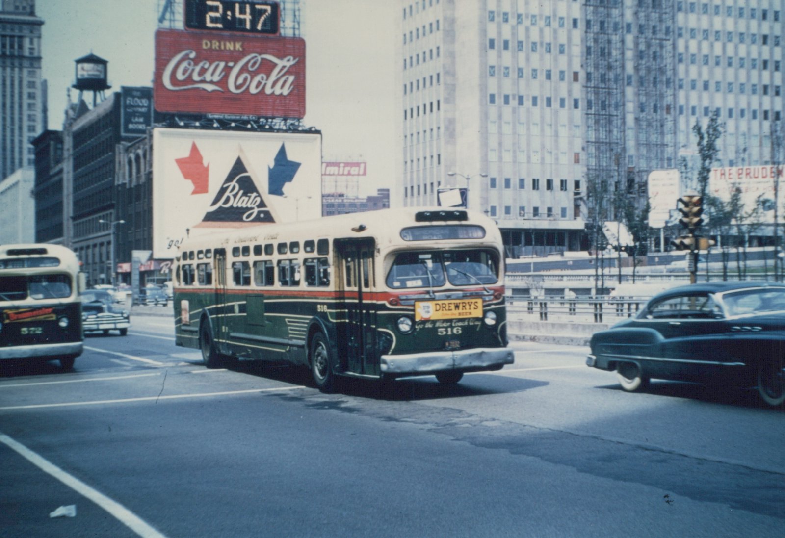 A vintage Chicago Transit Authority motor bus, number 516, is shown on a city street with other vehicles and large advertisements, including a Coca-Cola sign, under an overcast sky.