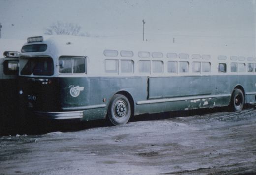 A side-view of a Chicago Transit Authority motor bus, numbered 500, painted in green and white, parked on a snow-covered lot with bare trees in the background.