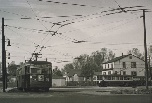 A black and white photo of two PCC streetcars on a Chicago street, with overhead wires and houses in the background.