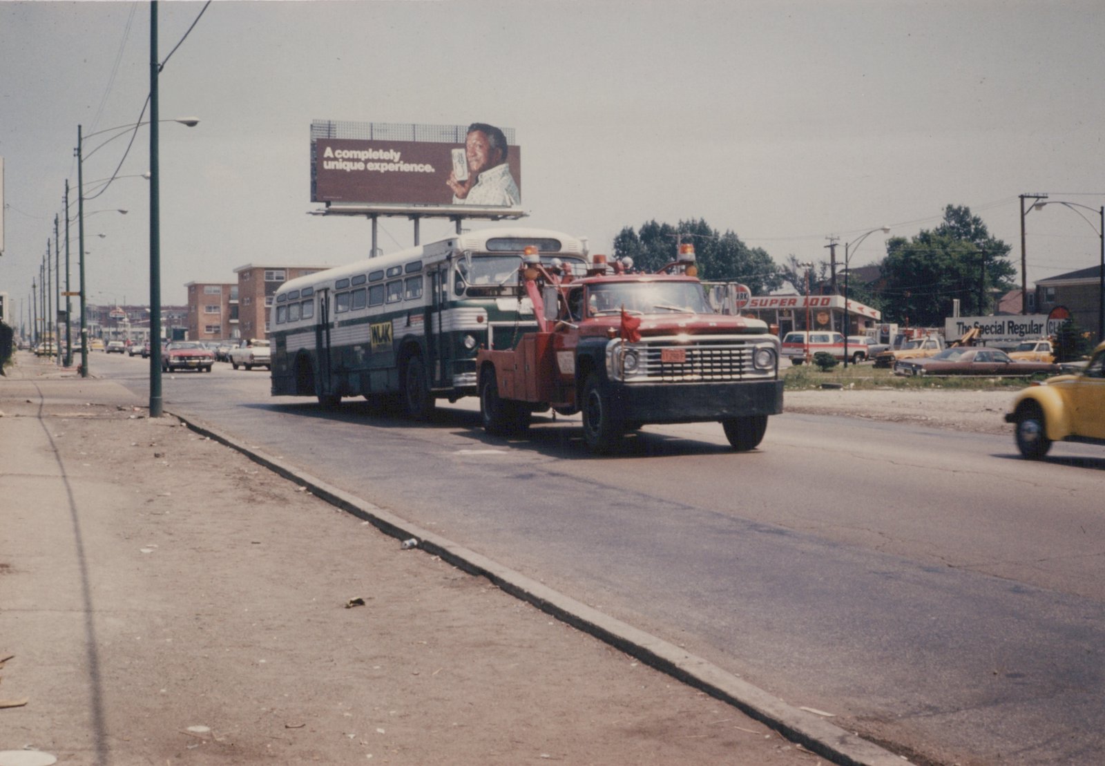 A green and white Chicago Transit Authority bus is being towed by a red tow truck on a city street, with a billboard and gas station in the background.