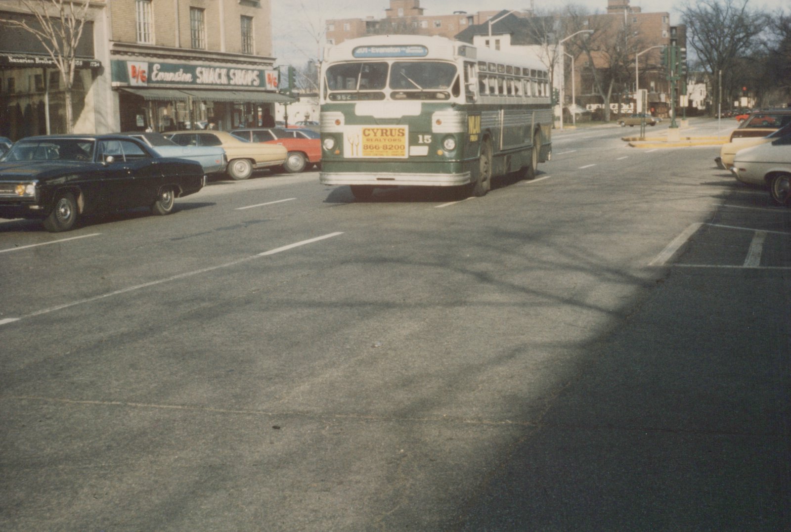 A vintage green and white CTA bus, number 952, is stopped on a city street lined with parked cars and storefronts, including an 'Evanston Snack Shops' sign, under a clear winter sky.