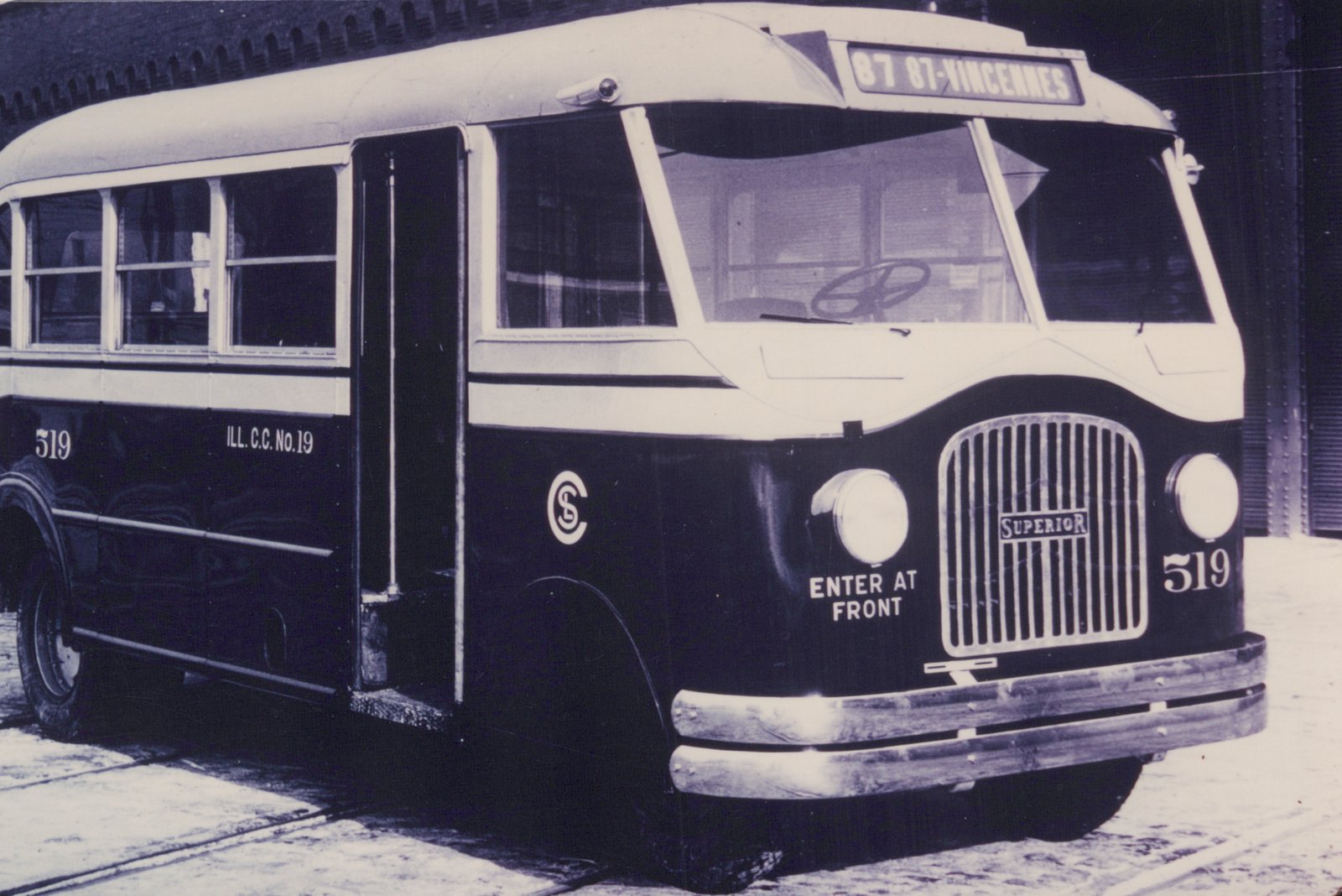 Black-and-white photo of a vintage Superior motor bus, number 519, with 'ILL. C.C. No. 19' on its side, parked on a city street with snow on the ground.