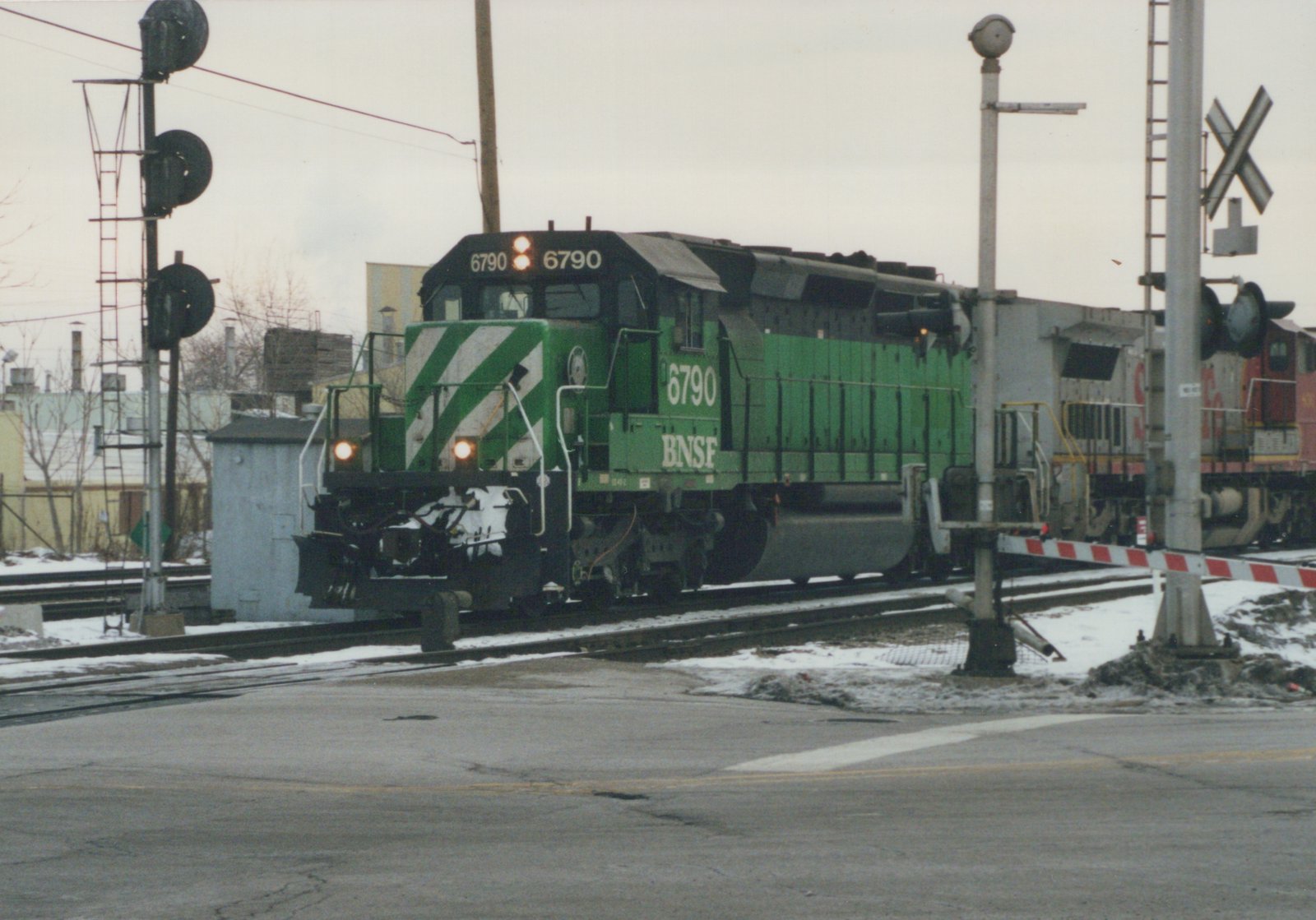 A green BNSF Railway diesel locomotive, number 6790, is stopped at a railroad crossing with snow on the ground.