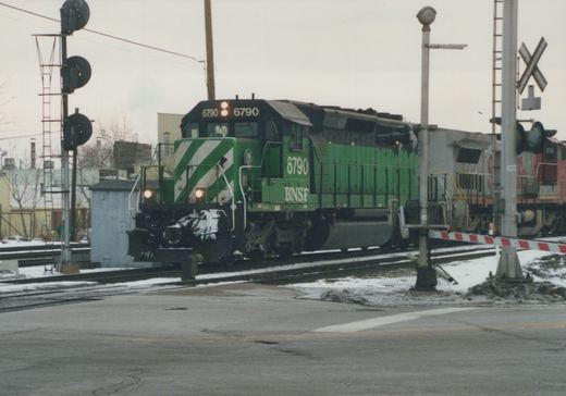 A green BNSF Railway diesel locomotive, number 6790, is stopped at a railroad crossing with snow on the ground.