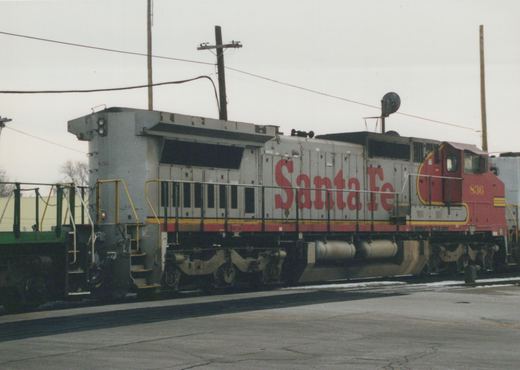 A gray and red Santa Fe diesel locomotive, number 836, is parked on tracks in a yard with snow on the ground.