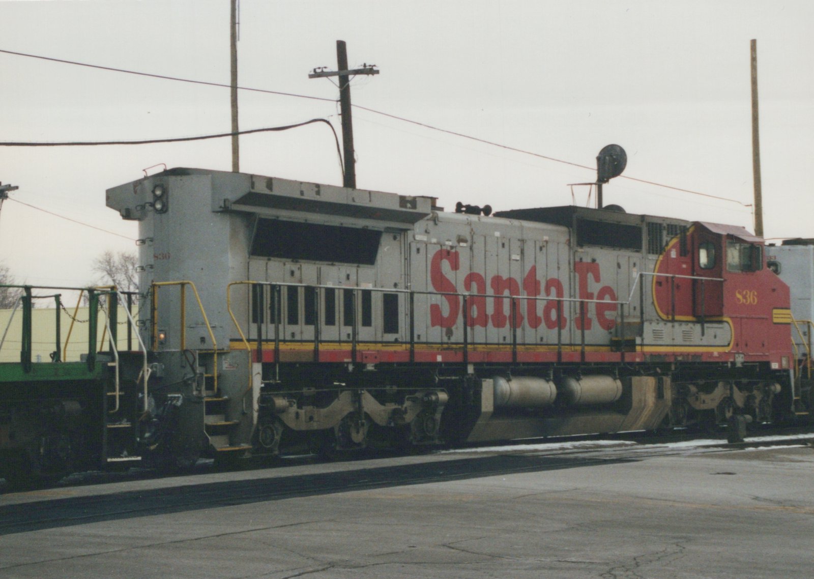 A gray and red Santa Fe diesel locomotive, number 836, is parked on tracks in a yard with snow on the ground.