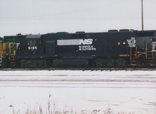 Side view of a black Norfolk Southern diesel locomotive numbered 5195 sitting on tracks in a snowy yard.