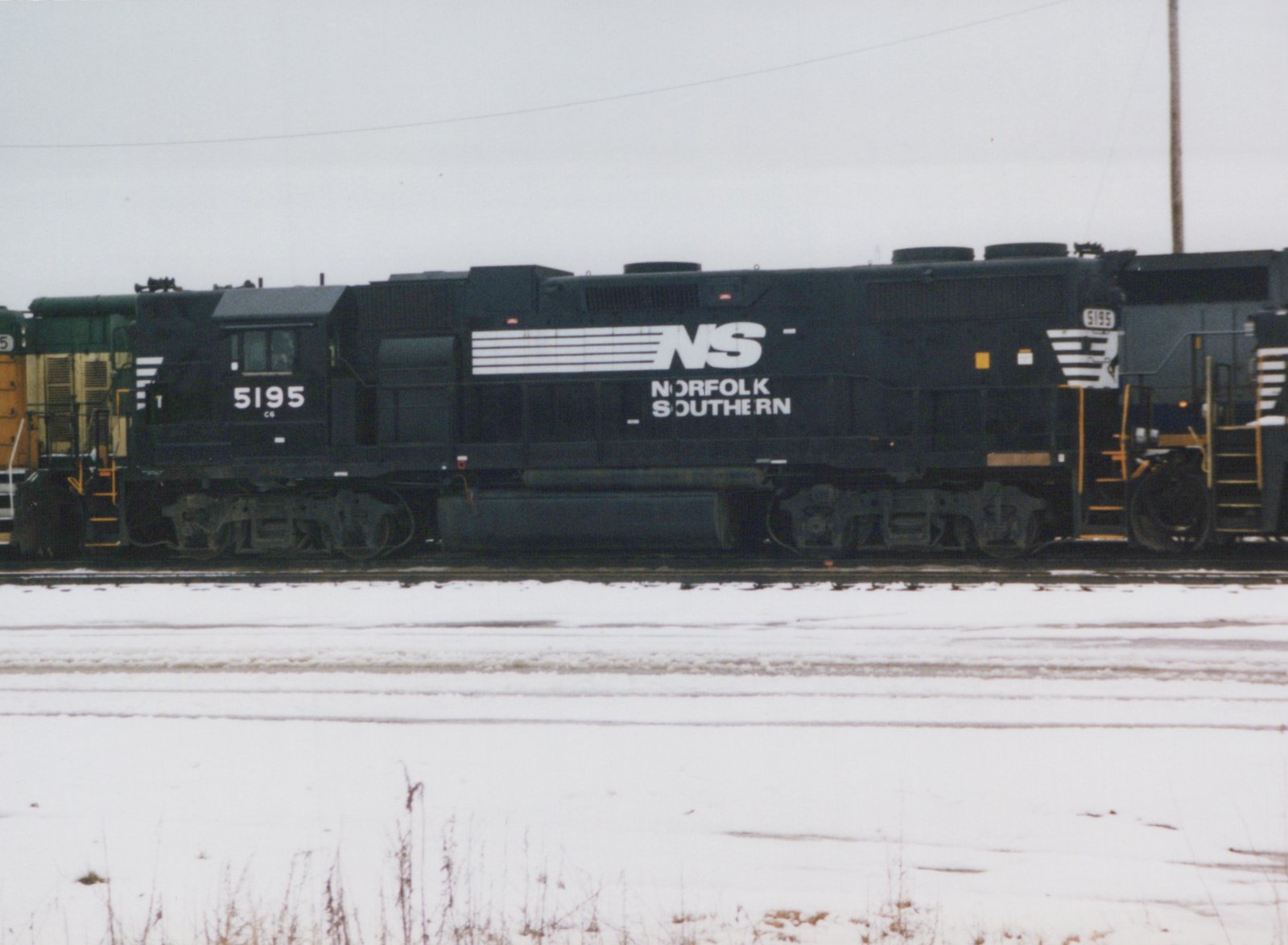 Side view of a black Norfolk Southern diesel locomotive numbered 5195 sitting on tracks in a snowy yard.