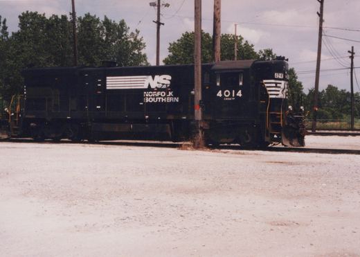 A black Norfolk Southern diesel locomotive, number 4014, is parked on tracks in a gravel yard with trees and utility poles in the background.
